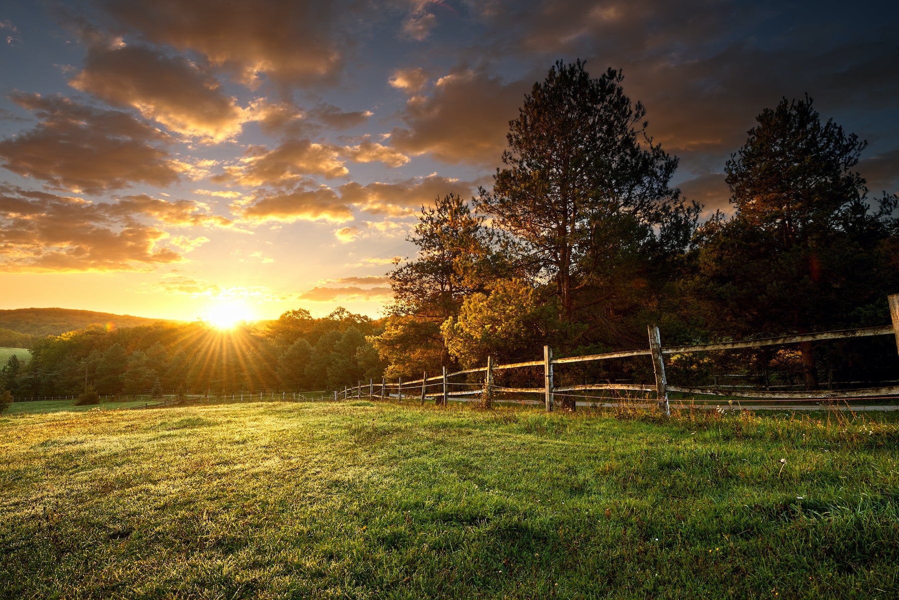 An image of a sunset over a field and a fence.